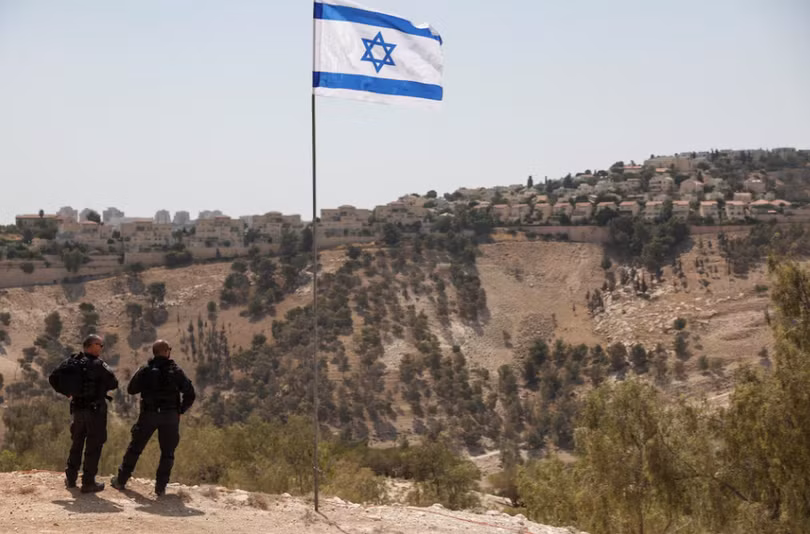 Lá cờ Israel tung bay, một phần của khu định cư Maale Adumim của Israel có thể được nhìn thấy ở phía sau, tại khu Bờ Tây do Israel chiếm đóng, ngày 14/8. Ảnh: Reuters.