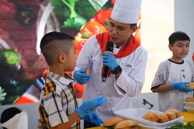 Chef tận tình hướng dẫn bé làm bánh mỳ. (Ảnh: VNA).