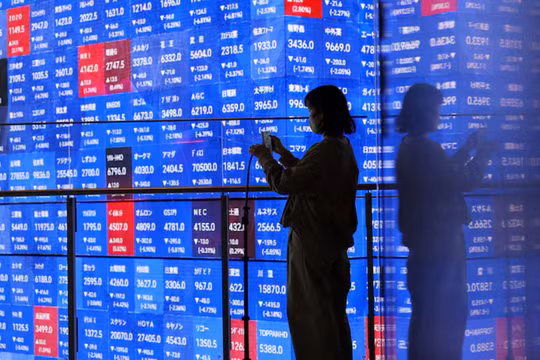 Một du khách đứng cạnh màn hình điện tử hiển thị bảng giá chứng khoán Nikkei của Nhật Bản bên trong một hội trường ở Tokyo, Nhật Bản, ngày 4/3. Ảnh: Reuters.