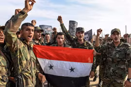 Quân đội chính phủ Syria giơ cao quốc kỳ và ảnh Tổng thống Assad tại ngoại ô thành phố Manbij hôm 15/10 (Ảnh: Newsweek)