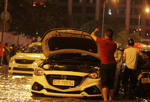 Hàng chục ôtô chết máy nằm giữa dòng nước ngập. Nhiều xe chết máy chắn ngang đường nên ùn ứ kéo dài cả km. Chủ xe phải gọi thợ, người nhà mang bình ắc quy đến thay.