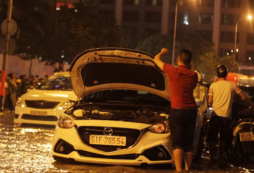 Hàng chục ôtô chết máy nằm giữa dòng nước ngập. Nhiều xe chết máy chắn ngang đường nên ùn ứ kéo dài cả km. Chủ xe phải gọi thợ, người nhà mang bình ắc quy đến thay.
