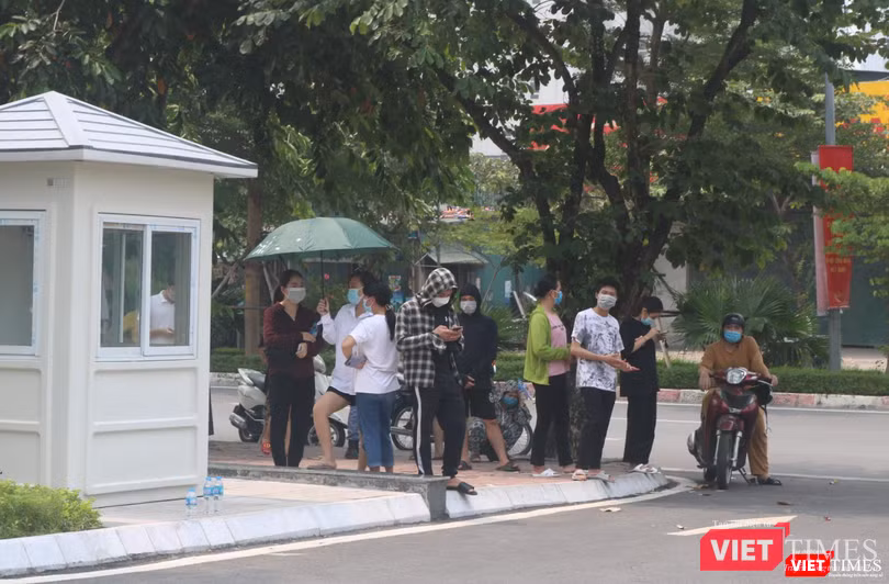 1 nhóm người tụ tập, đứng sát nhau trong 1 chiếc ô để tránh nắng và nói chuyện (Ảnh - Minh Thuý)