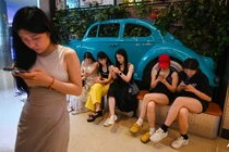 Người dân sử dụng điện thoại di động khi chờ chỗ trong một nhà hàng ở khu thương mại trung tâm Bắc Kinh ngày 11/7 (Ảnh: AFP)