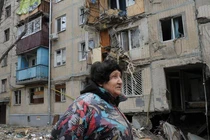 Một người phụ nữ đi qua tòa nhà bị hư hại do pháo kích ở Kharkiv, Ukraine (Ảnh: AP)