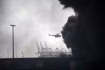 Một chiếc trực thăng bay qua làn khói đen bao trùm hiện trường vụ nổ tại cảng ở Iran, khiến ít nhất năm người thiệt mạng và hơn 700 người khác bị thương. Ảnh: AFP.