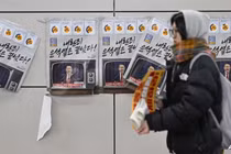 Một người phụ nữ đi ngang qua các tấm áp phích in hình Tổng thống Hàn Quốc Yoon Suk Yeol với dòng chữ "Tội phạm nổi dậy Yoon đã kết thúc" tại một ga tàu điện ngầm ở Seoul vào ngày 9/12. Ảnh: AFP.