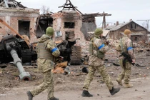 Quân đội Ukraine tái chiếm lại thị trấn Trostyanets hôm 26/3. Ảnh: những binh sĩ Ukraine đi ngang qua xác một chiếc xe tăng Nga giữa đống đổ nát (Ảnh: AP).