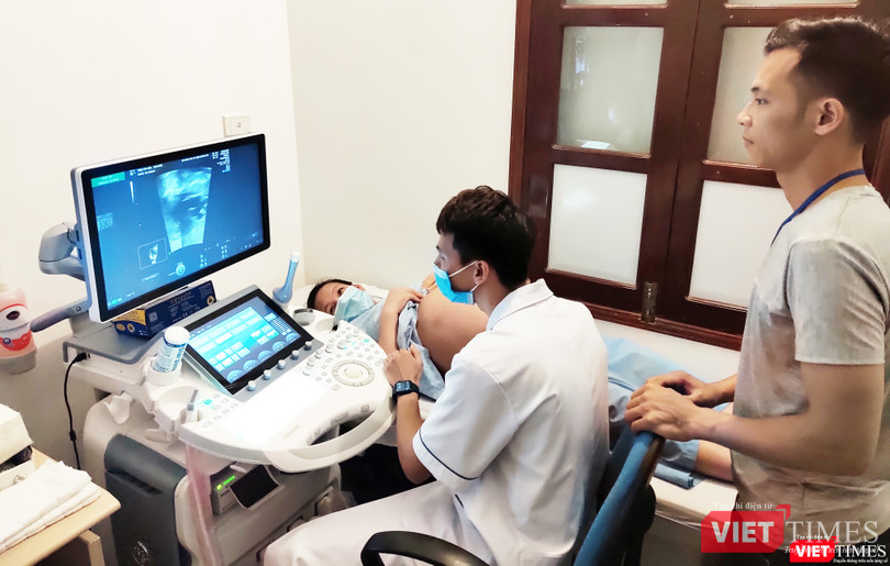 Bác sĩ tiến hành nội soi cho chị Liên (áo xanh đeo khẩu trang), chồng chị Liên anh Triệu Văn Sơn (áo xám) đứng cạnh dõi theo hình ảnh của 2 bé gái. Ảnh: Minh Thúy