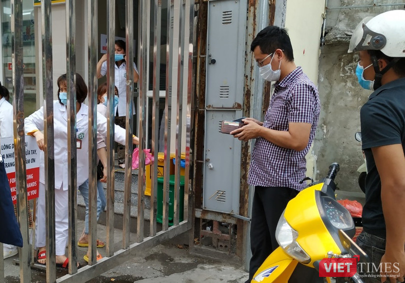 Người đàn ông áo kẻ lấy tiền để nhận số thuốc đựng trong nilon hồng từ tay nhân viên nhà thuốc tại cổng Bạch Mai trên phố Phương Mai.