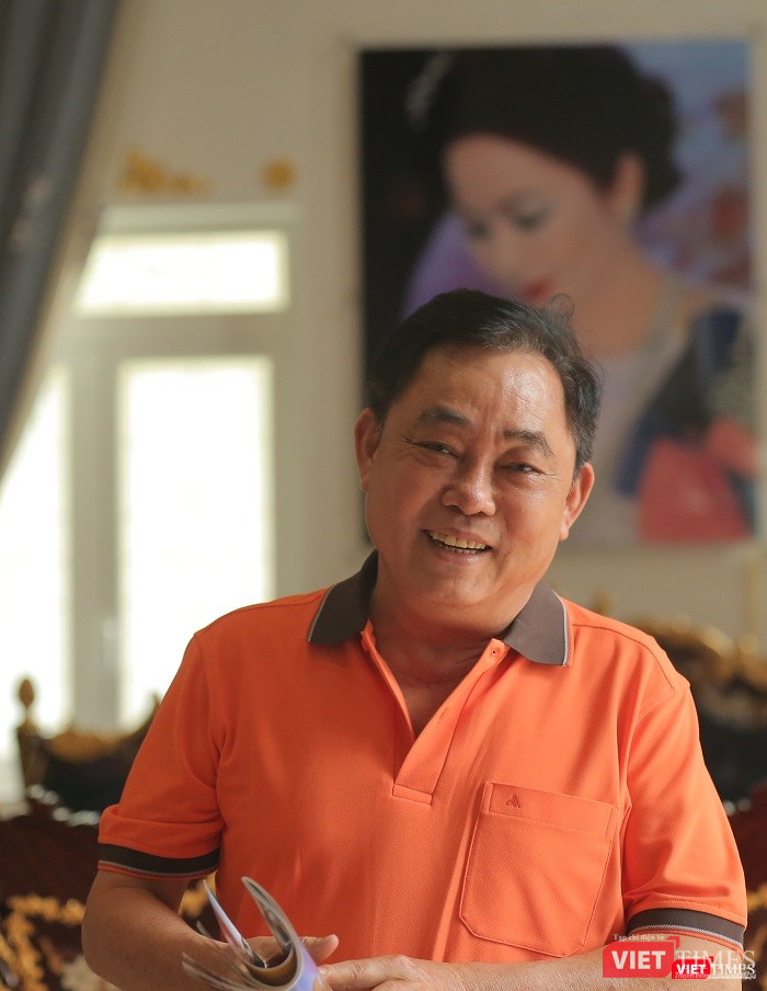 Ông Huỳnh Uy Dũng nét mặt rạng rỡ, phía sau là bức ảnh chân dung vợ treo trang trọng trên tường. Ảnh: An Tâm.