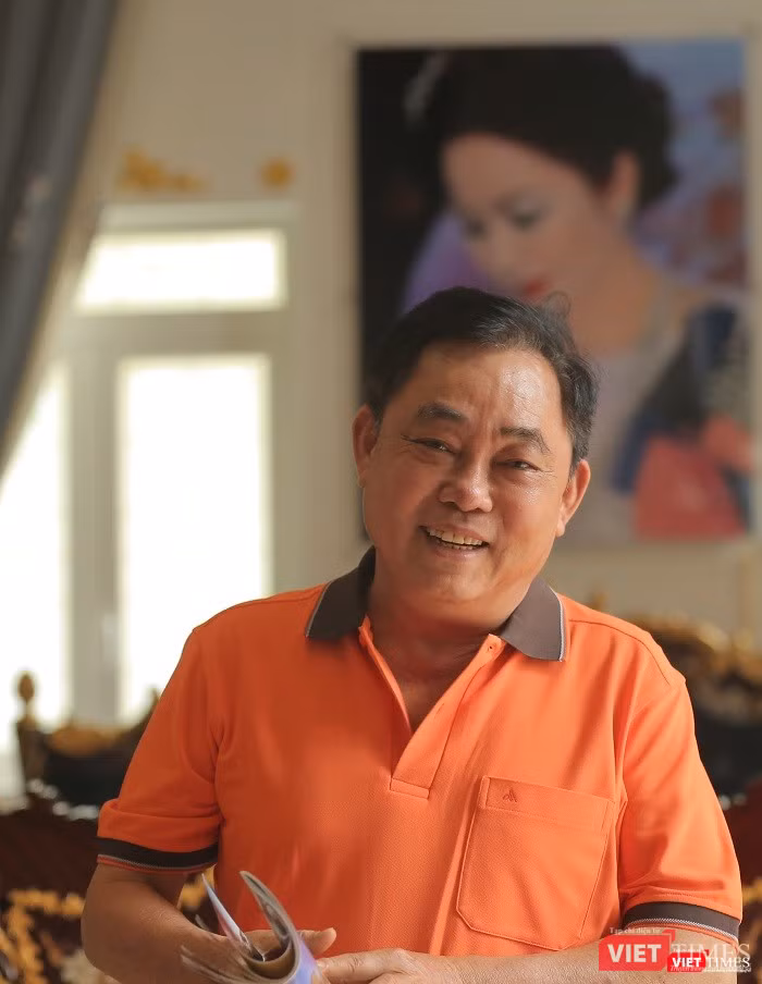 Ông Huỳnh Uy Dũng nét mặt rạng rỡ, phía sau là bức ảnh chân dung vợ treo trang trọng trên tường. Ảnh: An Tâm.