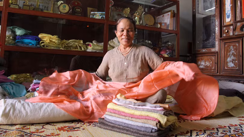 NNƯT Phan Thị Thuận và những thước lụa từ tơ tằm tại xưởng của bà. Với sự chăm chỉ, luôn mày mò sáng tạo bà đã nhận được rất nhiều bằng khen và giải thưởng trong nước về lĩnh vực tơ tằm. Ảnh: Thục Nhi