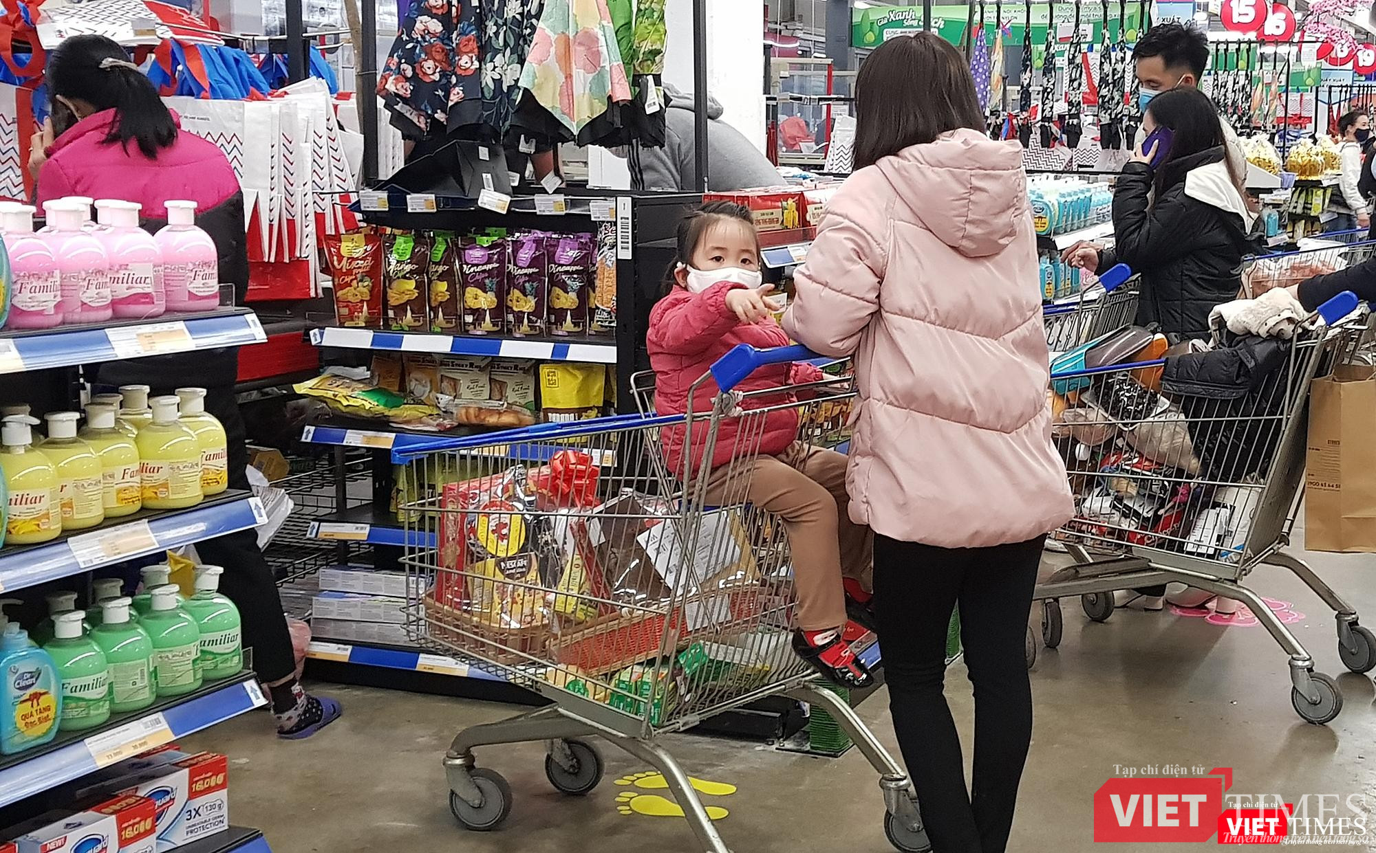Em bé này chỉ khoảng 3 tuổi, được mẹ đeo khẩu trang và đặt trên xe đẩy hàng