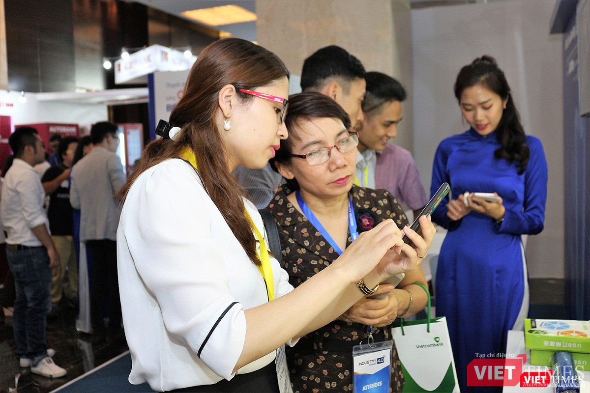 Nhân viên BIDV hướng dẫn khách tham quan cách sử dụng điện thoại để thanh toán hàng hóa qua mã QR code