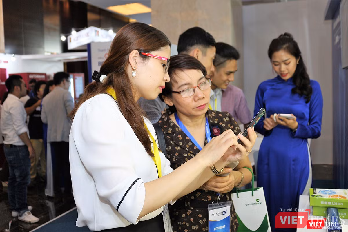 Nhân viên BIDV hướng dẫn khách tham quan cách sử dụng điện thoại để thanh toán hàng hóa qua mã QR code