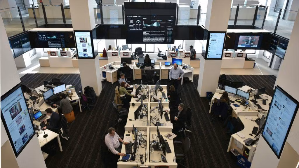 Các nhà báo tại The Washington Post làm việc trong văn phòng được bao quanh bởi màn hình lớn hiển thị trang báo và số lượng người đọc cập nhật