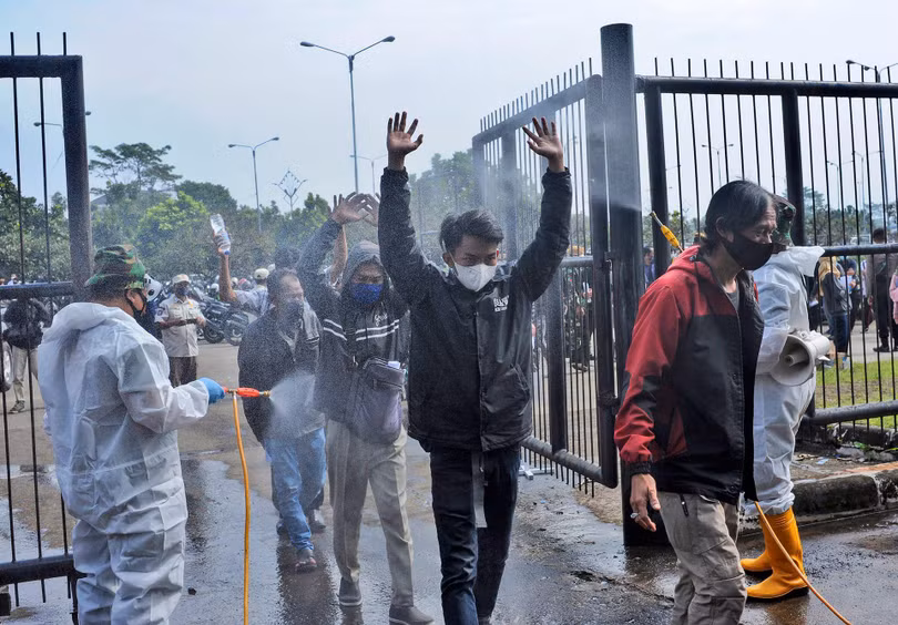 HNgày 17/6, trong đợt tiêm chủng hàng loạt ở Bandung, Tây Java, những người lính mặc quần áo bảo hộ đã phun thuốc khử trùng vào những người vào sân vận động để tiêm loại vaccine COVID-19 của Trung Quốc. (AP)