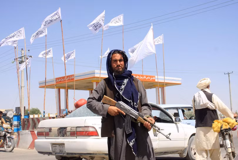 Một lính Taliban đứng gác trên phố Kabul, phía sau là các lá cờ của Taliban (Ảnh: Reuters).