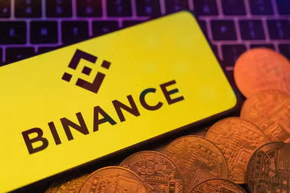Hình ảnh minh họa cho thấy một chiếc điện thoại thông minh có hiển thị logo Binance và hình ảnh các loại tiền mã hóa được đặt trên bàn phím. Ảnh: Reuters.