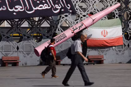 Người dân đi bộ bên cạnh mô hình tượng trưng của một tên lửa Iran và quốc kỳ Iran tại Quảng trường Imam Hussein ở Tehran, Iran, ngày 12/7. Ảnh: Reuters.