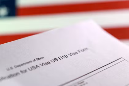 Một lá cờ Mỹ và một mẫu đơn xin thị thực H-1B. Ảnh minh họa: Reuters.