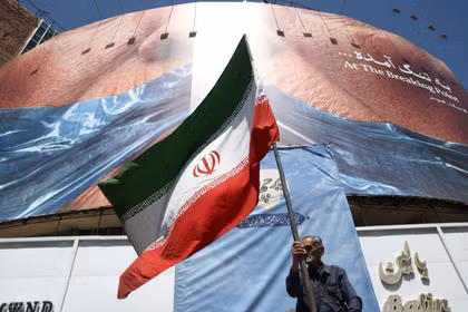 Một người đàn ông cầm cờ Iran gần một bảng quảng cáo chống Mỹ có hình Tổng thống Mỹ Donald Trump và eo biển Hormuz, tại Tehran, Iran, ngày 30/5. Ảnh: Reuters.
